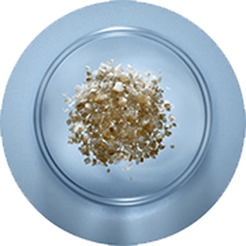 Zilvergrijze zoutkorrels op een glazen bord, tegen een lichte blauwe achtergrond.