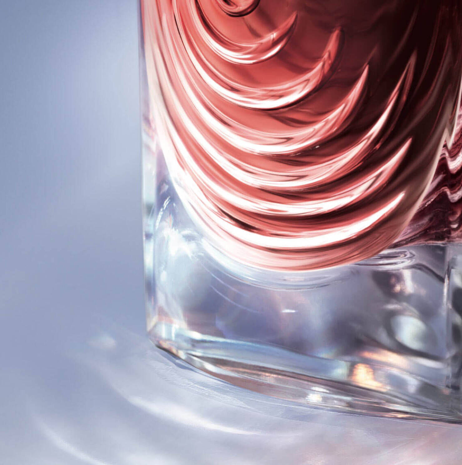 Close-up of a decorative glass bottle with a swirling, rose-colored design, reflecting light on a smooth surface.