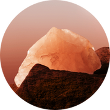 Een grote, doorzichtige kristalsteen in warme tinten, rustend op een groene ondergrond.