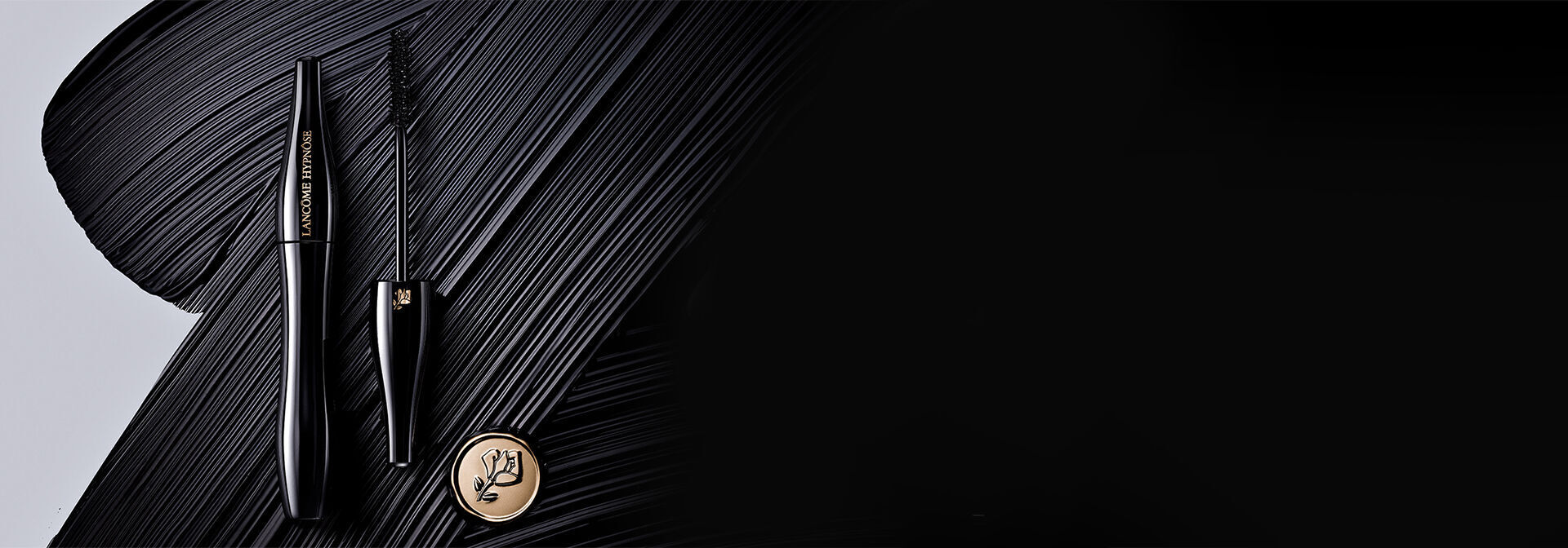 A sleek black mascara tube and wand are positioned against a dramatic black brushstroke background, featuring a gold logo prominently displayed.