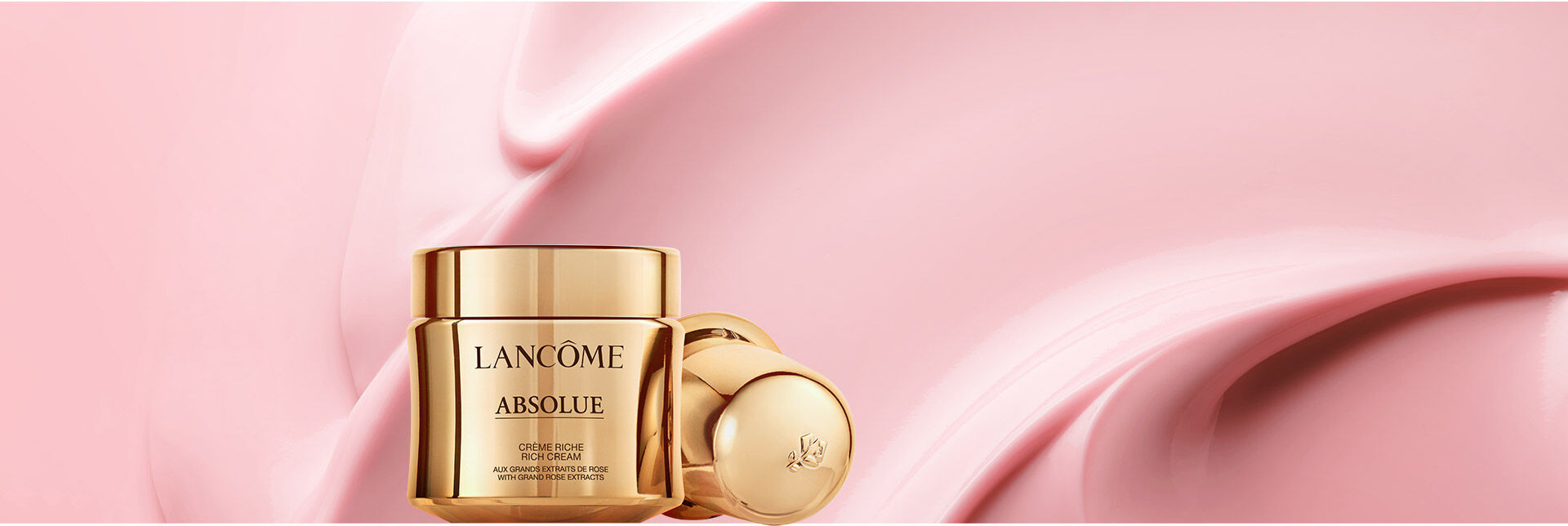 A luxurious gold jar of Lancome Absolue cream against a soft pink background, with a smooth, creamy texture swirled beside it.