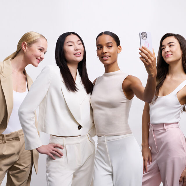 Vier vrouwen poseren samen voor een selfie, gekleed in stijlvolle, neutraalgekleurde outfits.