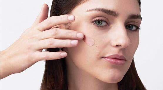 Une femme maquille sa joue avec un produit de beaute, regardant la camera.