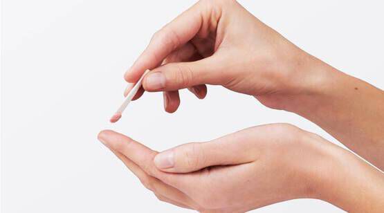 Une main tient un batonnet appliquant une creme ou un produit sur la paume de l'autre main.