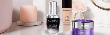 Een selectie van Lancome huidverzorgings- en make-upproducten op een stijlvolle ondergrond, waaronder een serum, foundation en een anti-aging creme, naast een kaars.