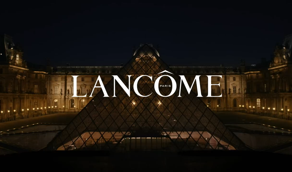 Festivallicht verlicht de glazen piramide van het Louvre, met de naam "Lancome" prominent in het midden.
