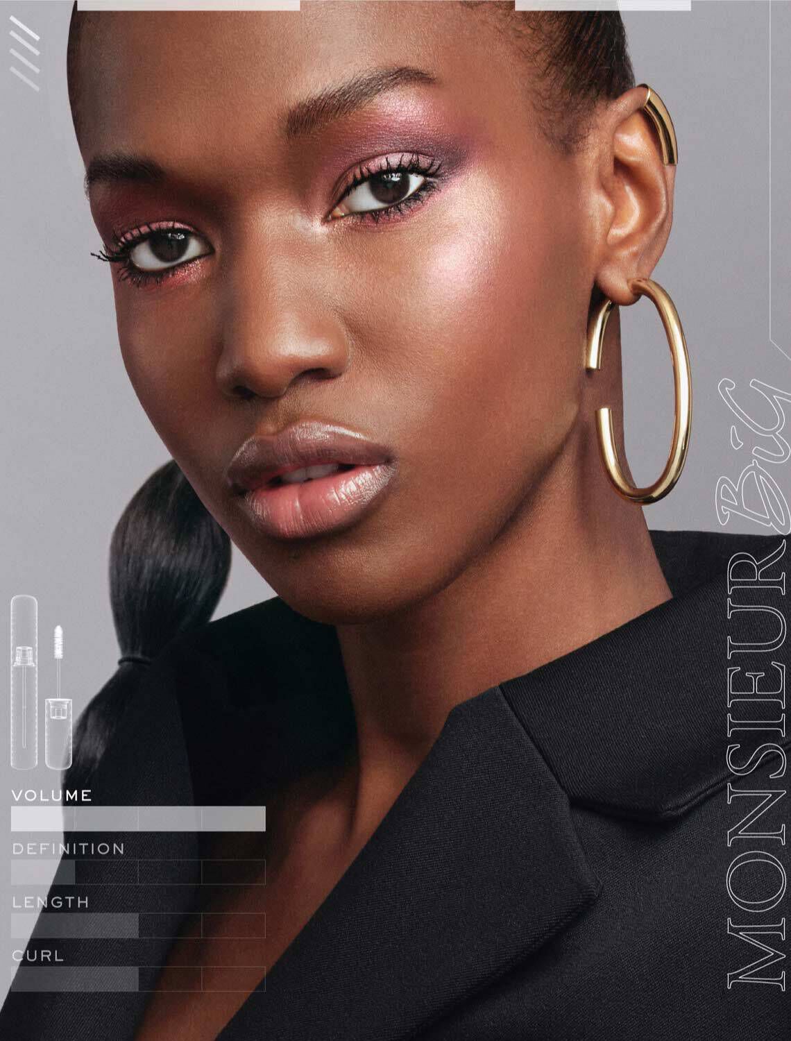Model met een stralende huid en goudkleurige oorbellen, met een glamoureuze make-uplook. Naast haar zijn er tekstlabels die "Volume," "Definitie," "Lengte" en "Krul" aangeven.