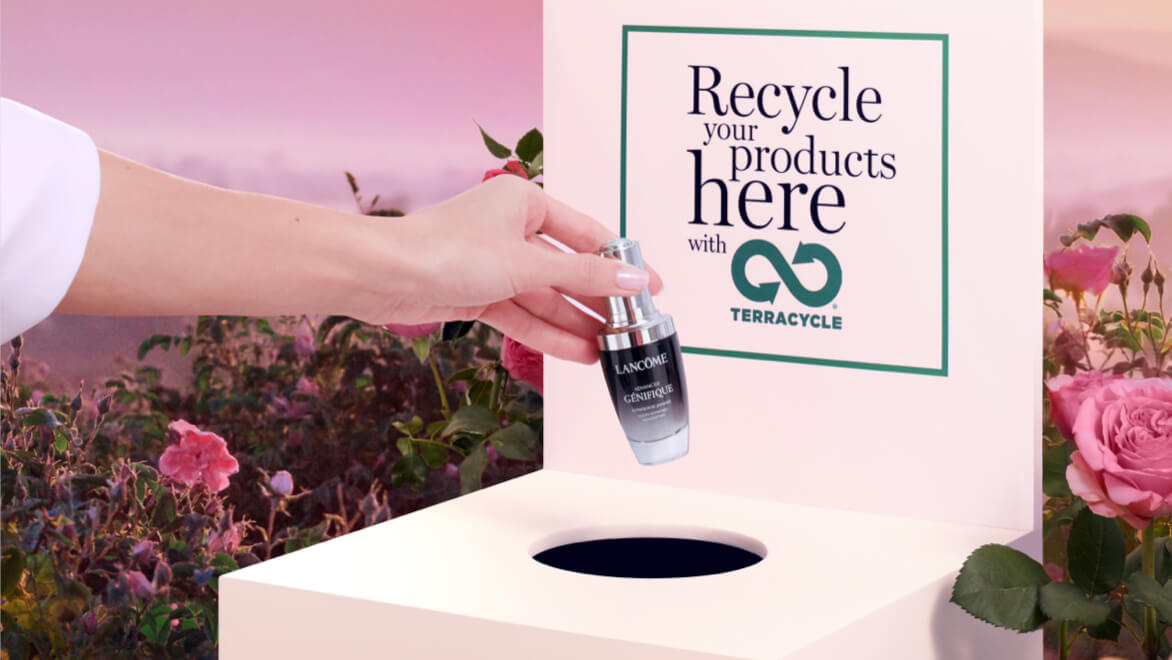 Hand plaatst een Lancome-serum in een recyclingdoos van Terracycle, omringd door rozen.